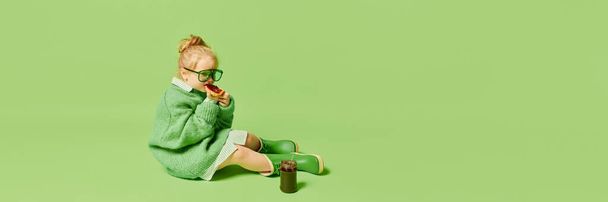 Happy smiling cute kid, little girl in fashionable look clothes and sunglasses posing over light green background. Spring fashion collection, happiness, ad concept. Monochrome portrait - Foto, immagini