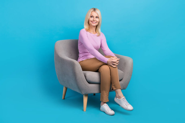 Volledige lengte foto van vrolijke mooie dame zitten comfort stoel kijken lege ruimte kantoormeubilair geïsoleerd op blauwe kleur achtergrond. - Foto, afbeelding