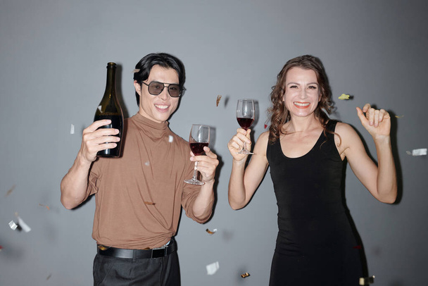 Pozytywni ludzie pijący wino i tańczący pod spadającym konfetti na imprezie - Zdjęcie, obraz