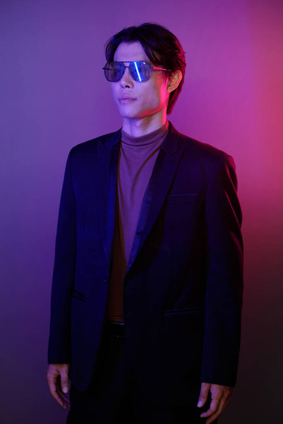 Portrait of confident young man in suit and sunglasses standing against pink and purple background - Foto, Imagen