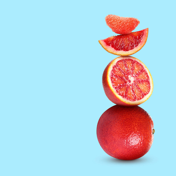 Stacked cut and whole red oranges on pale light blue background, space for text - Foto, Bild