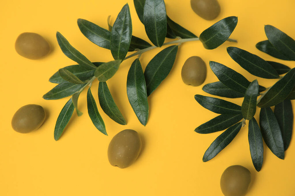 Fresh olives and green leaves on yellow background, flat lay - Фото, зображення