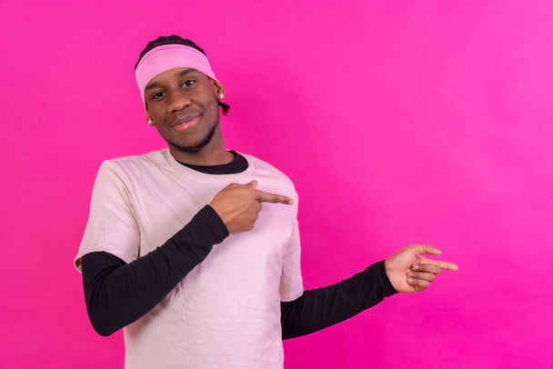 Black ethnic man in pink clothes on a pink background, pointing to a free right copy space - Fotoğraf, Görsel