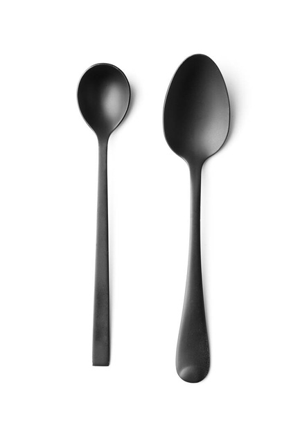 Black matte metal spoons on a white background top view, black cutlery on white insulation. - Foto, Imagen