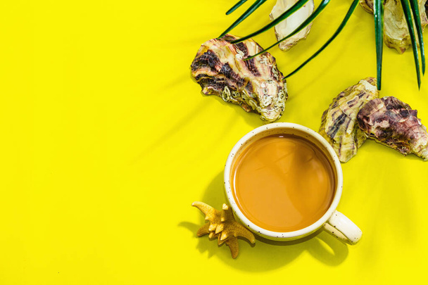 Una tazza di caffè in stile marino. Stella marina, ostriche, foglie di palma. Dura luce, ombra scura, sfondo giallo brillante, lay flat, vista dall'alto - Foto, immagini