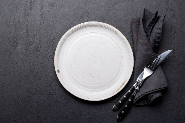 Empty plate with fork and knife on dark stone table. Flat lay with copy space - Foto, Imagen