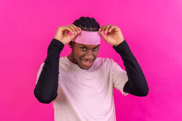Black ethnic man in pink clothes on a pink background, concept portrait, putting on the headband - Fotó, kép