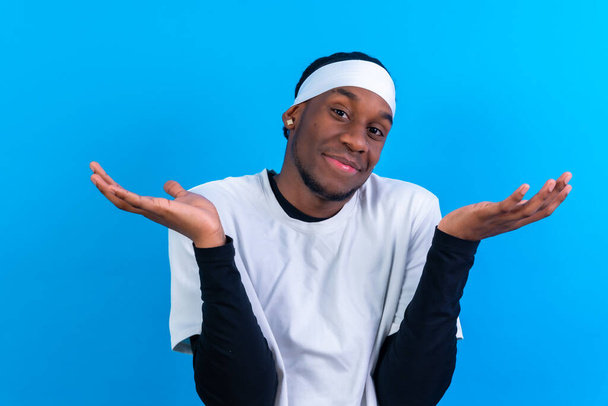 Black ethnic man in white clothes on a blue background, gesture of I don't care and happy - Фото, изображение