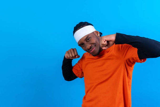 Black ethnic man in orange clothes on a blue background, smiling and having a good time dancing - Фото, изображение