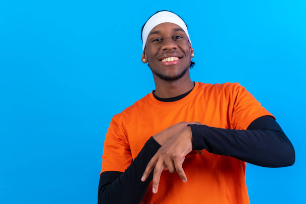 Black ethnic man in orange clothes on a blue background having fun smiling and dancing - Foto, imagen
