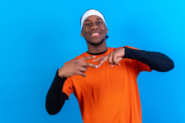 Black ethnic man in orange clothes on a blue background having fun smiling and party dancing - Fotoğraf, Görsel