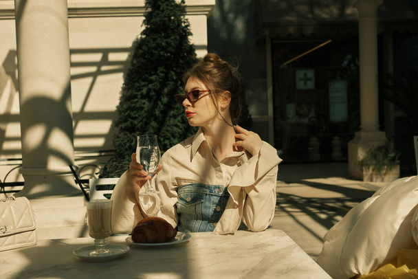 Una ragazza seduta in un caffè che tiene un bicchiere d'acqua nella mano destra - Foto, immagini