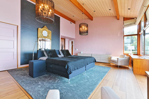 una camera da letto con pareti rosa e pavimenti in legno, insieme a un letto nero in camera ha un tappeto blu sul pavimento - Foto, immagini
