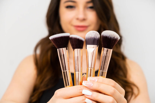 Attractive young woman holding golden makeup brushes. Professional makeup artist concept.  - Fotó, kép