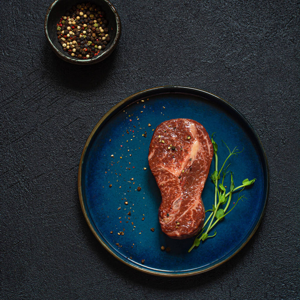 Roh marmoriertes Rindersteak auf Teller, fertig zum Kochen mit Mikrogemüse. Die Form des Steaks ist Glühbirne. Ernährungsenergiekonzept für den Menschen, Draufsicht, Minimalismus. - Foto, Bild
