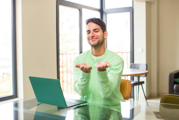 young hispanic man smiling happily with friendly, confident, positive look, offering and showing an object or concept. working at home - Foto, Imagen