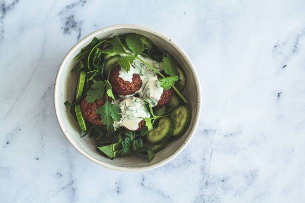 Green salad with falafel, tahini dressing in a white bowl on a white marble background. Alternative vegan recipe. - Foto, Bild