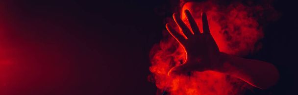 man smokes a hookah in a bar and blows out a large cloud of smoke with red neon lighting - Фото, изображение