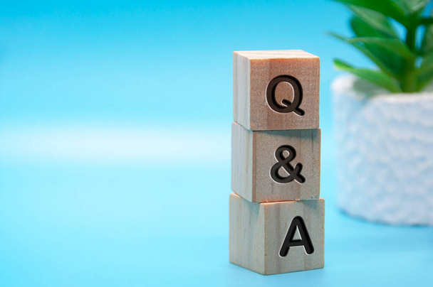 QとAテキストは、ライトブルーとテーブル植物の背景を持つ木製のブロックに刻まれた。質問と答えの概念。スペースのコピー. - 写真・画像