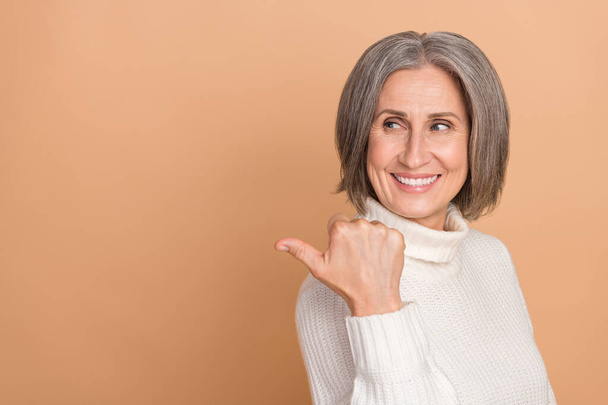 Photo portrait of promoter middle aged senior woman point finger look empty space recommend new stomatology isolated on beige color background. - Φωτογραφία, εικόνα