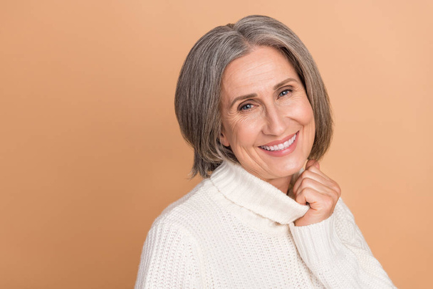 Portrait photo of cheerful optimistic lady grandmother touch collar knitted white sweater enjoy winter clothes isolated on beige color background. - Φωτογραφία, εικόνα