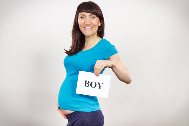 Happy smiling pregnant woman holding white card with inscription boy. Expecting for newborn. Extending family - Foto, imagen
