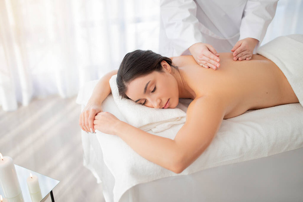 Beautiful Young Indian Female Resting In Spa Salon During Massage Session, Attractive Woman Lying On Table With Closed Eyes, Enjoying Beauty Treatments And Wellness Procedures, Free Space - Foto, Imagen