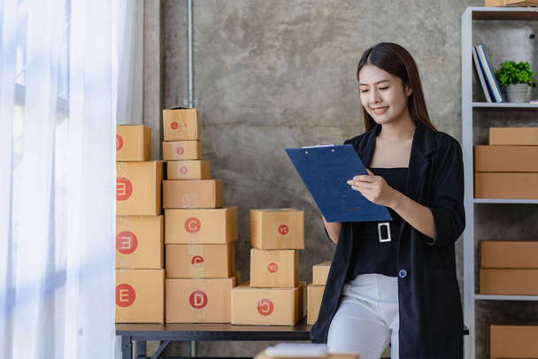 Asijská mladá žena pracující z domova s krabicemi, kontrola objednávek a příprava doručit balíčky, MSP on-line obchodní koncept - Fotografie, Obrázek