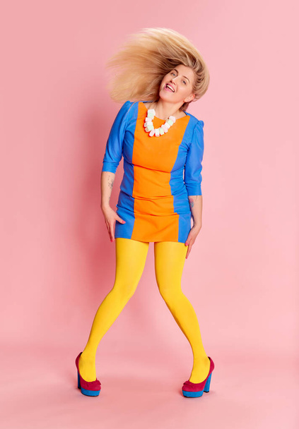 Full-length portrait of happy smiling woman in colorful clothes with yellow tights on heels posing against pink studio background. Concept of emotions, facial expression, lifestyle and fashion - Fotografie, Obrázek