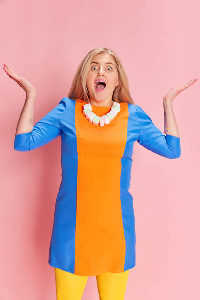 Shocked and excited face. Portrait of woman in colorful clothes with marshmallow necklace emotionally posing against pink studio background. Emotions, facial expression, lifestyle and fashion concept - 写真・画像