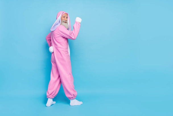 Side profile full size photo of cheerful elderly pensioner wear pink bunny costume demonstrating biceps isolated on blue color background. - Foto, afbeelding