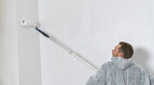 junger Maler, der mit einem Farbroller die Wand eines Raumes bemalt. Do it yourself Konzeptbild mit Kopierraum - Foto, Bild