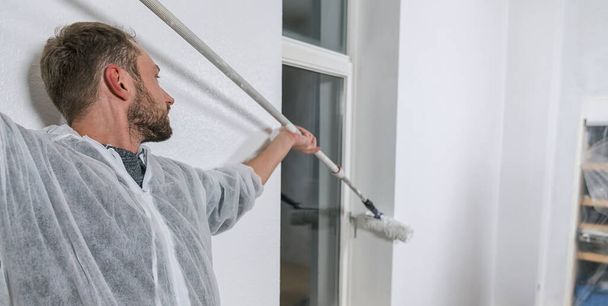 pintor que trabaja con rodillo de pintura para pintar la esquina de una ventana de la habitación con color blanco. hágalo usted mismo imagen concepto - Foto, Imagen