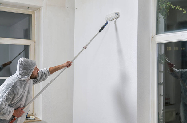 pintor que trabaja con rodillo de pintura para pintar la pared de una habitación. hágalo usted mismo imagen concepto  - Foto, Imagen