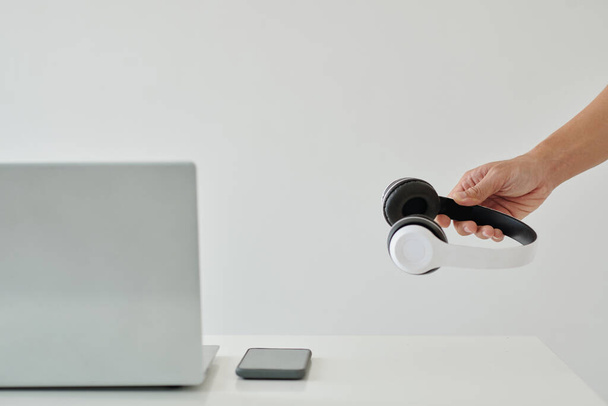Mão de homem de negócios colocando fones de ouvido na mesa de escritório com laptop e smartphone - Foto, Imagem