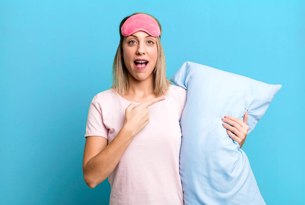 pretty blonde woman looking excited and surprised pointing to the side. pajamas and nightwear concept - Photo, Image
