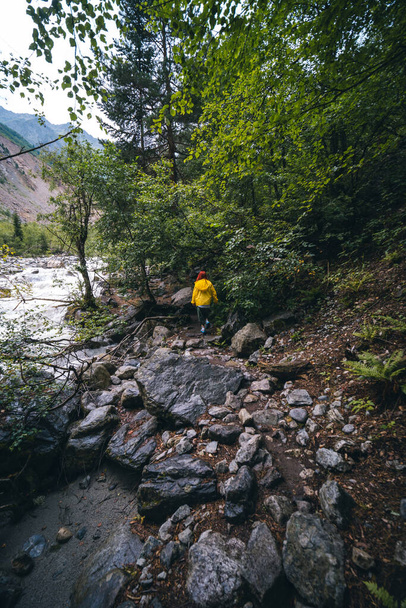Mujer de chaqueta amarilla, sendero turístico hasta el glaciar Chalaadi. en el fondo turbulento flujo del río, Georgia, Mestia. Concepto de viajes y vacaciones. - Foto, imagen