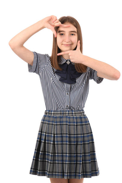 Joven chica hermosa en un uniforme escolar sobre un fondo blanco, sonriendo haciendo marco con las manos y los dedos con la cara feliz. Concepto de creatividad y fotografía. - Foto, imagen