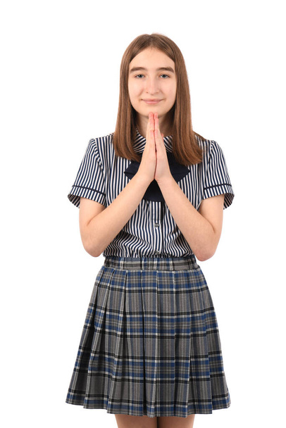 Joven chica hermosa en un uniforme escolar sobre un fondo blanco, orando con las manos juntas pidiendo perdón sonriendo confiado. - Foto, imagen