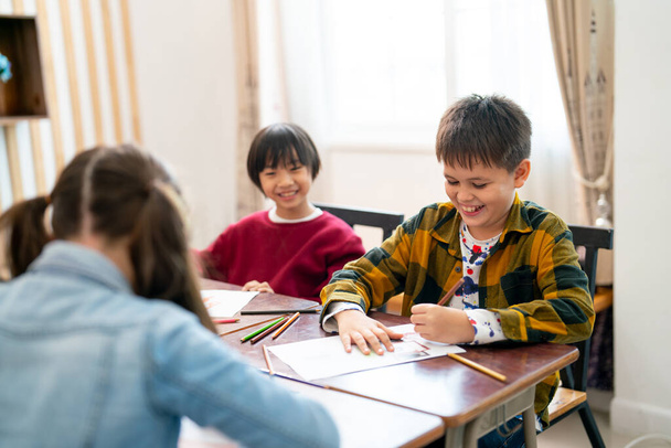 Mały azjatycki chłopiec wygląda szczęśliwy z uśmiechem i patrzeć na swojego przyjaciela rysować i malować obraz w klasie w szkole w koncepcji wolności twórczej dla dzieci. - Zdjęcie, obraz