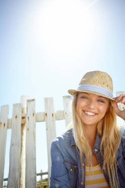 Woman, hat and portrait in sunshine, blue sky background or mockup lens flare. Summer fashion, park and female relax at field fence, nature and freedom with happiness in environment, mock up or smile. - Foto, afbeelding