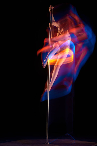 Sensual dancer. Young girl performing pole dance isolated over black studio background with mixed neon lights. Concept of sport and dance, beauty of movements, action, modern style - Zdjęcie, obraz
