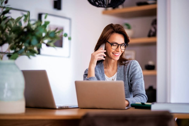 Happy woman using mobile phone and laptops for work. Confident business woman working from home. Home office.  - Φωτογραφία, εικόνα
