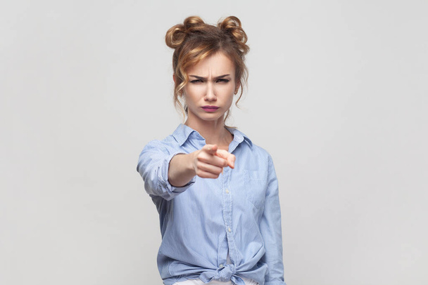 You are guilty in my misfortune. Displeased blonde woman blaming someone, pointing directly at camera, making serious face, wearing blue shirt. Indoor studio shot isolated on gray background. - Photo, Image