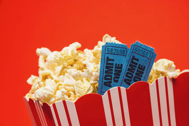 popcorn in striped box with two tickets to the cinema on red background - Foto, imagen