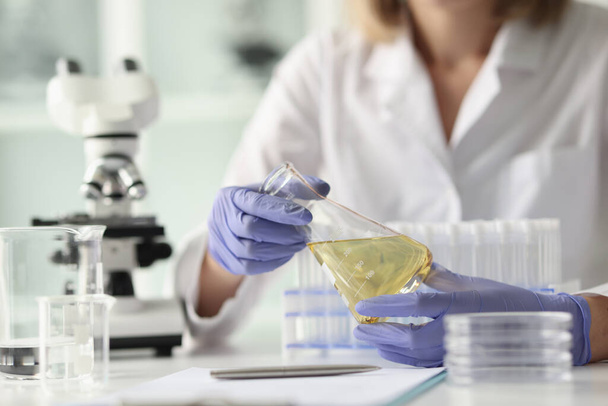 A tudós a kutatólaborban ül, és flaskát tart a kezében. Női vegyész végez kísérleteket a laborban. - Fotó, kép