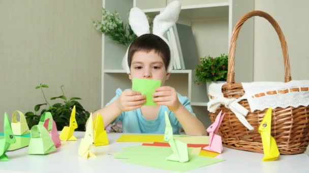 Garçon d'âge préscolaire avec des oreilles de lapin tête de chiffon fait de l'artisanat de Pâques, figurines origami de lapins et paniers de papier. - Séquence, vidéo