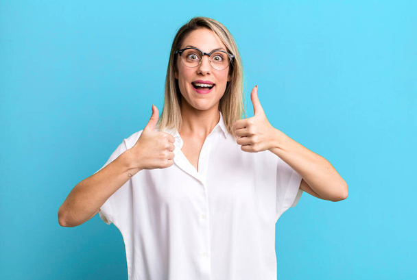 blonde adult woman smiling broadly looking happy, positive, confident and successful, with both thumbs up - Фото, изображение