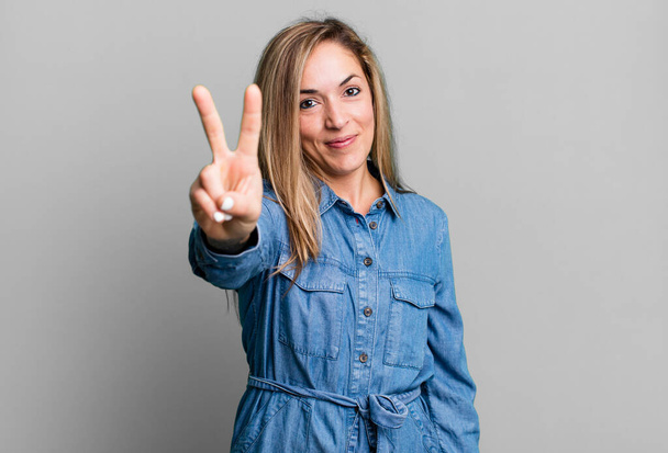 blonde adult woman smiling and looking happy, carefree and positive, gesturing victory or peace with one hand - Zdjęcie, obraz