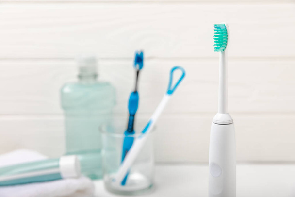 Electronic ultrasonic toothbrush, mouthwash, floss, tongue cleaner and toothpaste on white wooden background. Items for dental care and caries prevention in the bathroom. Dentistry concept. Copy space. - 写真・画像
